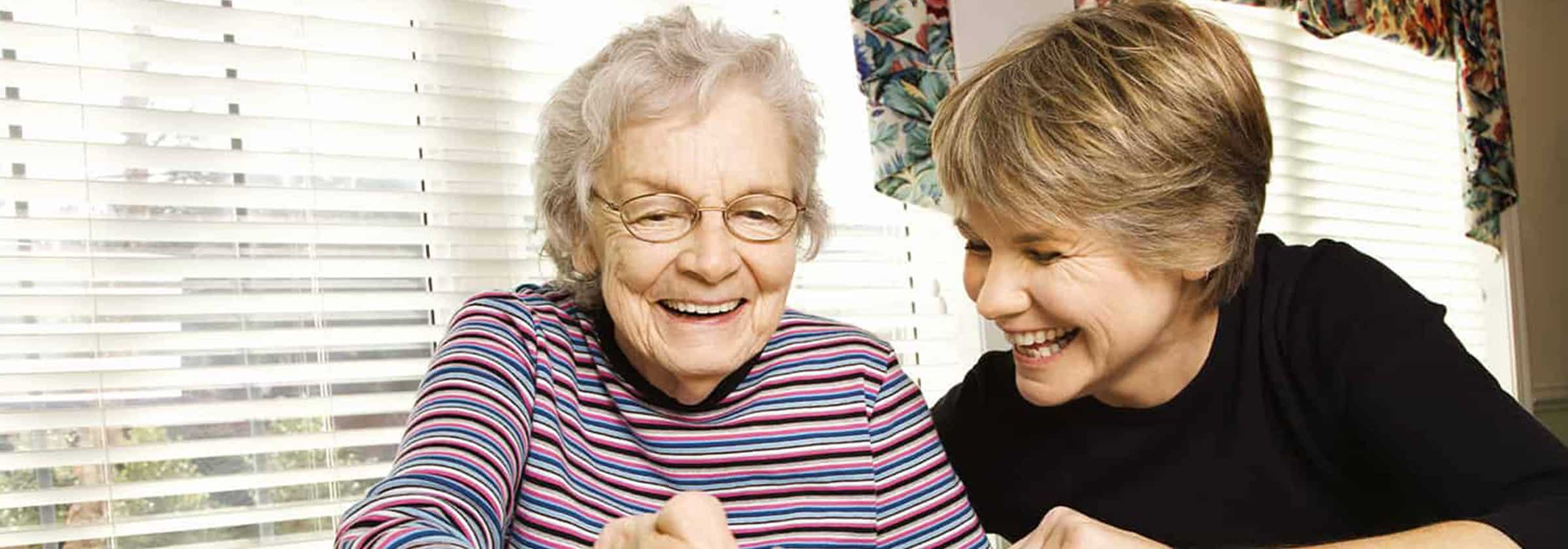 An elderly senior living resident in memory care smiling as a woman sits beside her smiling