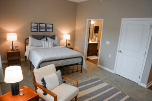 Bedroom with a bed, chair and rug and an open door to another room.