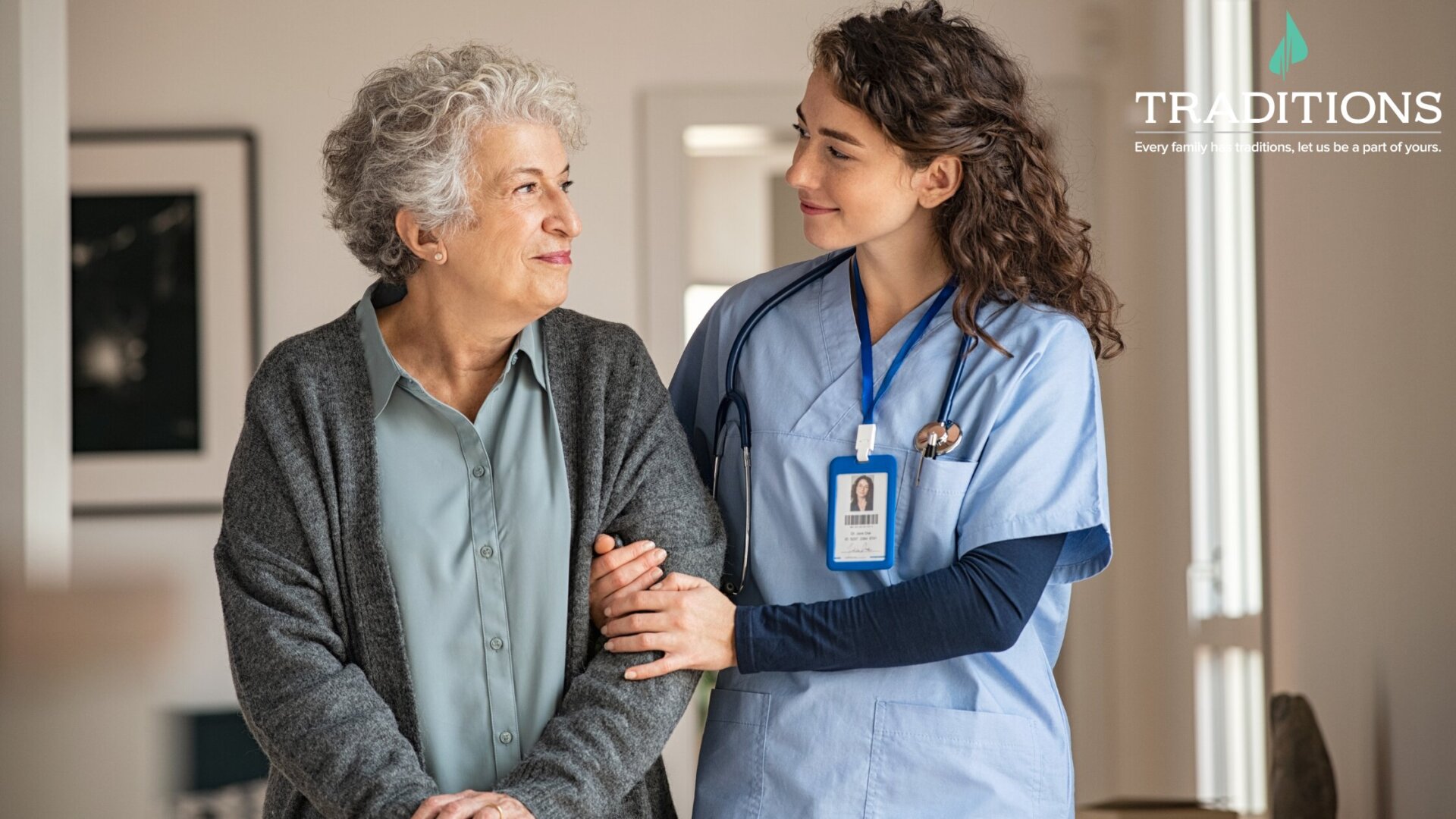 A senior woman standing and looking over at her female nurse who is stabilizing her to help her on a walk at Traditions of Lebanon in Lebanon, OH.