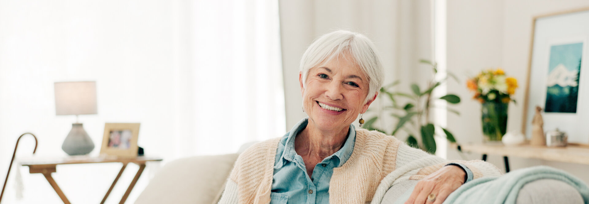 Elderly woman sitting on a couch with a warm welcoming smile.
