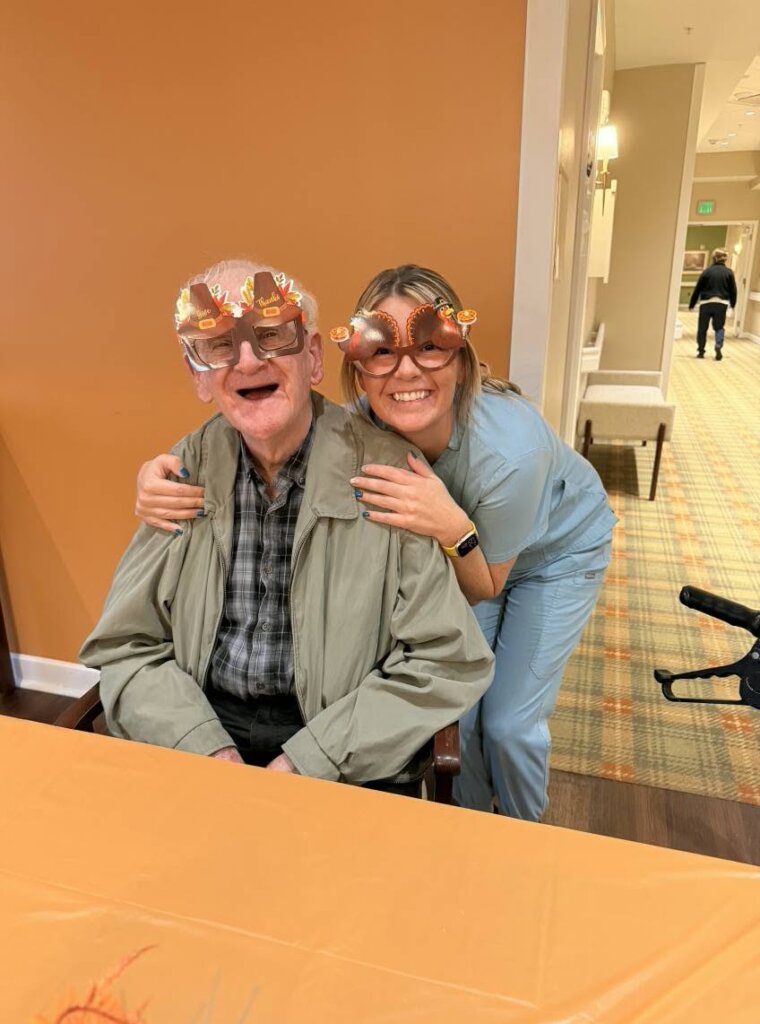 Resident and nurse share a smile while wearing festive Thanksgiving glasses at Traditions of Lebanon's Thanksgiving Dinner